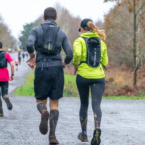 Coureurs sur un large chemin forestier de la forêt de Rennes, jambes couvertes de boue